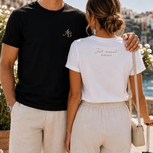 Może przedstawiać: Czarny t-shirt ze złotym monogramem AB na piersi oraz biały t-shirt ze złotym napisem Just married i datą 18.08.2026 nadrukowanymi na plecach. Obie koszulki mają krótkie rękawy i okrągły dekolt, zestawione z beżowymi spodniami.
