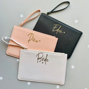 Peut inclure: Trois pochettes avec des lettres dor&eacute;es. Les pochettes sont blanches, roses et noires. La pochette blanche dit "Bride", la pochette rose dit "Dina" et la pochette noire dit "Eden".