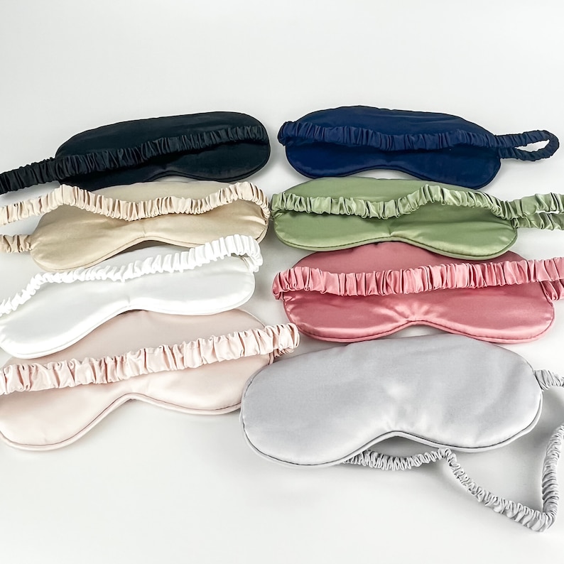 May include: A set of ten silk sleep masks in various colors, including black, navy blue, beige, green, pink, and gray. The masks are all made of soft, smooth silk and have an elastic band that goes around the head.