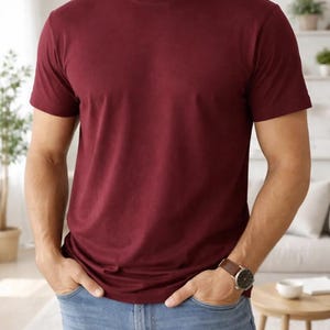Pode incluir: Uma camiseta bord&ocirc; com gola redonda. A camiseta de manga curta &eacute; de cor lisa e &eacute; combinada com jeans azul claro. Um rel&oacute;gio de couro marrom &eacute; vis&iacute;vel no pulso.
