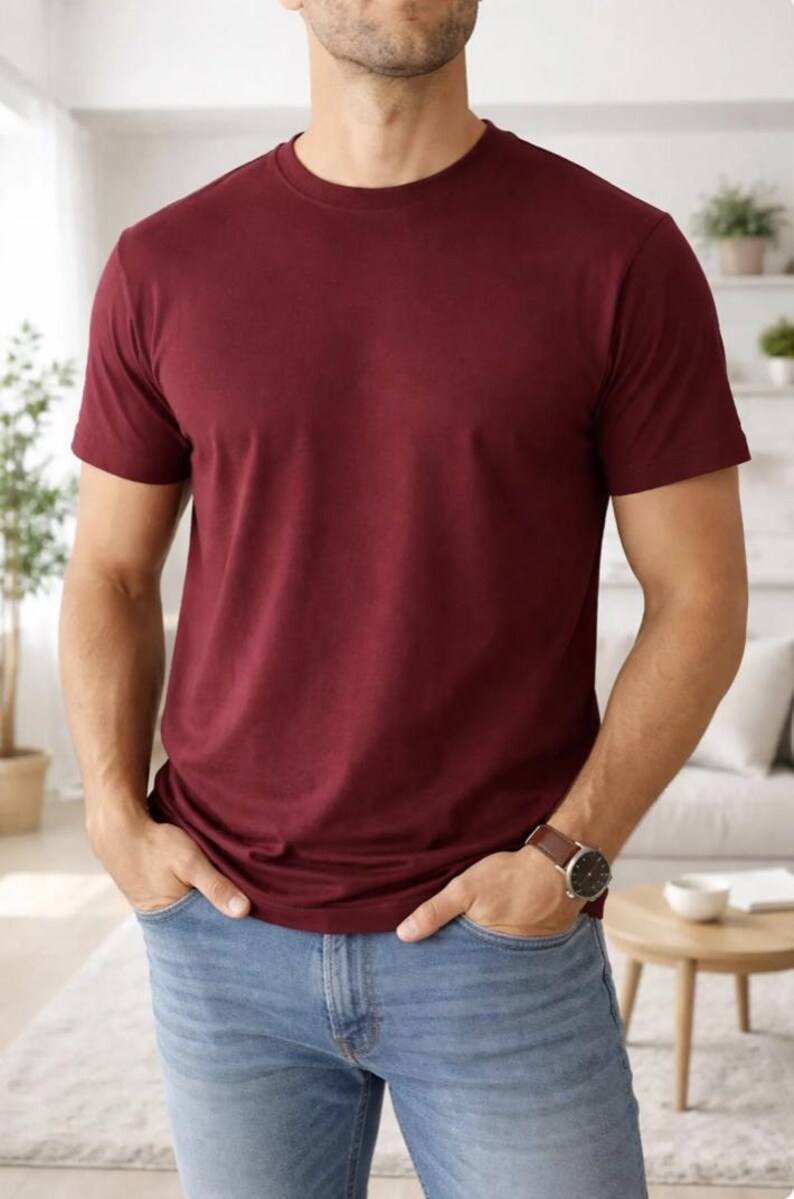 Pode incluir: Uma camiseta bord&ocirc; com gola redonda. A camiseta de manga curta &eacute; de cor lisa e &eacute; combinada com jeans azul claro. Um rel&oacute;gio de couro marrom &eacute; vis&iacute;vel no pulso.
