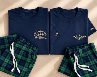 May include: Two sets of navy blue pajamas featuring green and navy plaid pants with white drawstring ties. The shirts have gold text: one reads "all I want for Christmas..." and the other "is you" with a heart and the letters B and T.