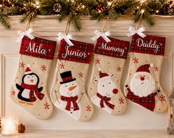 May include: Four beige Christmas stockings with red and green plaid cuffs, each featuring a white satin bow and a name embroidered in white script. The stockings display appliqued characters: a penguin, a snowman, a reindeer, and Santa Claus.