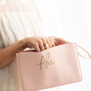 May include: A pink zippered pouch with a gold inscription that reads "Alecia" with a small heart symbol.