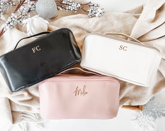 May include: Three zippered pouches with personalized lettering. The pouches are black, white, and pink. The black pouch has the initials "FC" in gold lettering. The white pouch has the initials "SC" in gold lettering. The pink pouch has the name "Melissa" in gold lettering.