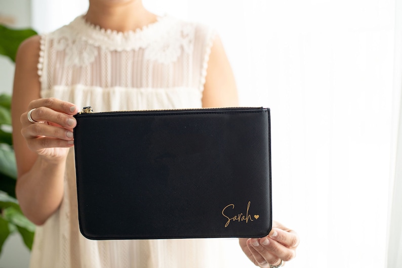 May include: A black zippered pouch with a gold zipper and the name "Sarah" written in gold script with a small gold heart.