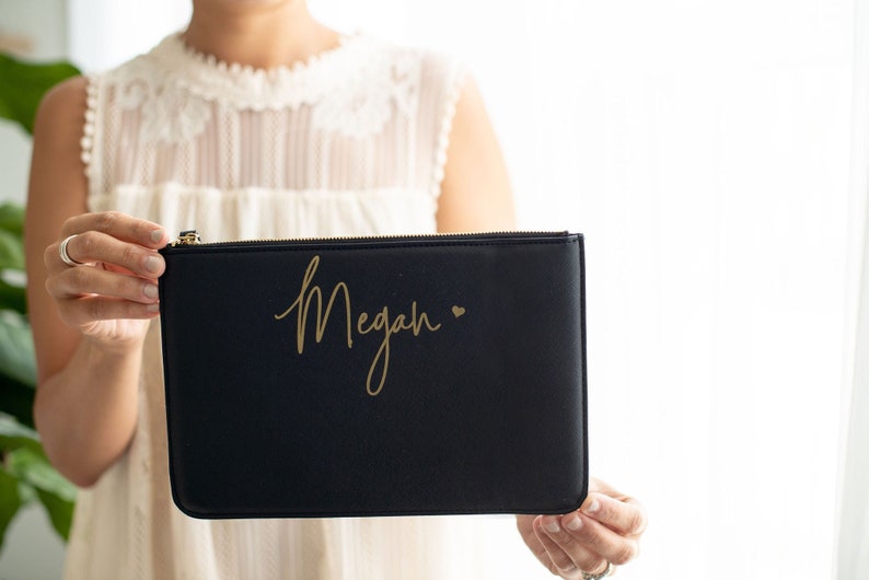 May include: A black zippered pouch with a gold inscription that reads "Megan" with a small gold heart.