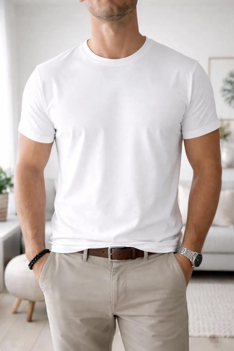 Pode incluir: Uma camiseta branca lisa com gola redonda. A camisa &eacute; combinada com cal&ccedil;as c&aacute;qui e um cinto de couro marrom. Uma pulseira de contas pretas e um rel&oacute;gio prateado s&atilde;o vis&iacute;veis.