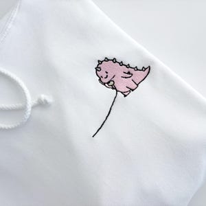 May include: White hoodie with a pink embroidered dinosaur holding a balloon.