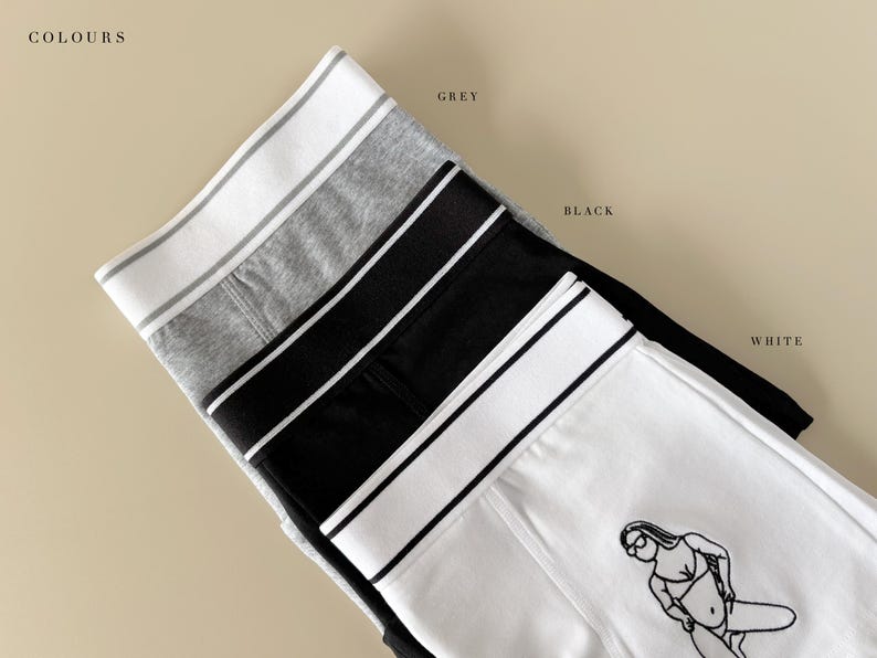 May include: Four pairs of underwear in different colors: grey, black, white, and white with a black line drawing of a woman. The underwear has a wide elastic waistband with a stripe.