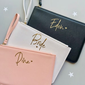 Peut inclure: Trois pochettes zipp&eacute;es avec des lettres dor&eacute;es. Les pochettes sont noires, blanches et roses. La pochette noire dit "Eden" avec un c&oelig;ur. La pochette blanche dit "Bride" avec deux c&oelig;urs. La pochette rose dit "Dina" avec un c&oelig;ur.