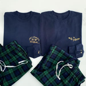 May include: Two navy blue long-sleeved shirts with gold text. One shirt says "All I want for Christmas..." with a small Christmas tree graphic. The other shirt says "is you" with a snowflake and two hearts. Two pairs of green and blue plaid pajama pants.