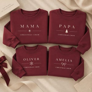 Peut inclure: Quatre sweat-shirts à col rond rouge foncé avec du texte blanc et des icônes de vacances. Les hauts portent les inscriptions MAMA, PAPA, OLIVER et AMELIA, suivies du texte CHRISTMAS CREW et d'un symbole unique comme une étoile, un sapin, un flocon ou un nœud.