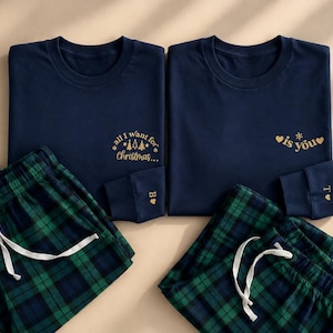 Op de afbeelding: Twee donkerblauwe shirts met lange mouwen en twee groen met donkerblauw geruite pyjamabroeken. Het linker shirt heeft de gouden tekst all I want for Christmas, het rechter shirt is you. Elke mouwboord heeft een gouden letter en een hartje.