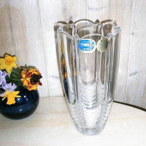 May include: A clear glass vase with a fluted design and a Bohemian Crystal label. The vase is sitting on a light wood surface.