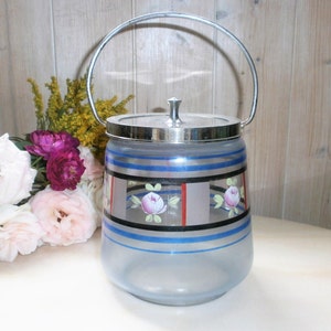 May include: A vintage glass ice bucket with a silver handle and rim. The bucket has blue and silver horizontal stripes, with a floral design of pink roses. The lid has a silver knob. The bucket is frosted glass.