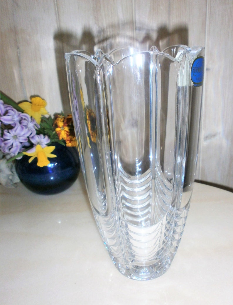 May include: A clear glass vase with a textured design. The vase has a wide mouth and a narrow base. The vase is made by the company "Cristal d'Arques".