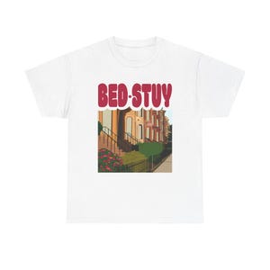 May include: White t-shirt with a red graphic of a row of brownstone houses with the text "BED-STUY" in red.