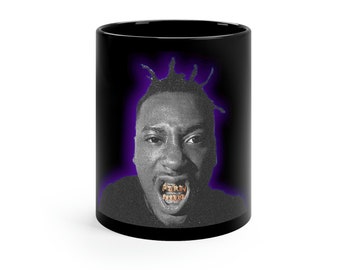 Puede incluir: Taza de cerámica negra con una imagen en blanco y negro de un hombre con una parrilla dorada, sobre un fondo morado.