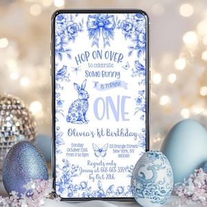 Könnte beinhalten: Eine blaue und weiße florale Handy-Einladung zu einem ersten Geburtstag. Die Einladung zeigt ein Kaninchen, die Worte "Hop on Over to celebrate Some Bunny is turning One" und den Text "Olivia's 1st Birthday".