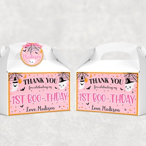 May include: Two white gable boxes with handles, decorated for a Halloween-themed first birthday. Each box features a pink and orange label with the text "THANK YOU for celebrating my 1ST BOO-THDAY. Love, Madison." A round sticker on top says "Madison".