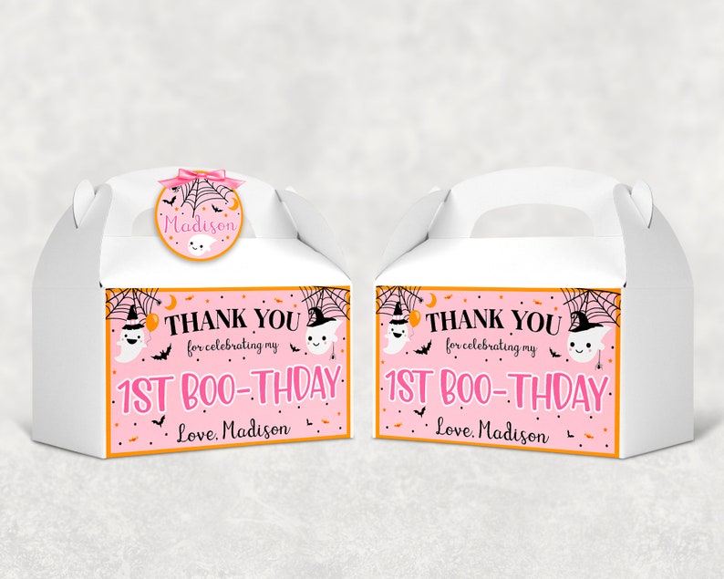 May include: Two white gable boxes with handles, decorated for a Halloween-themed first birthday. Each box features a pink and orange label with the text "THANK YOU for celebrating my 1ST BOO-THDAY. Love, Madison." A round sticker on top says "Madison".