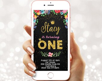 May include: A smartphone displaying a digital birthday invitation on a black background with gold glitter accents, floral borders, and the text: Stacy is turning ONE, August 5th at 6pm, Our House, 658 Charlie Ennls Rd, Dyersburg, RSVP 556-774-8875.