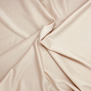 May include: A close-up of a smooth, beige fabric with soft folds and wrinkles. The fabric has a subtle sheen and a luxurious feel.