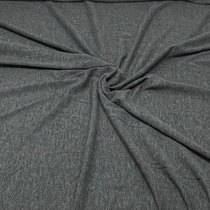 May include: Close-up of a dark grey fabric with a textured, slightly speckled surface. The fabric is folded and draped, creating soft folds and wrinkles.