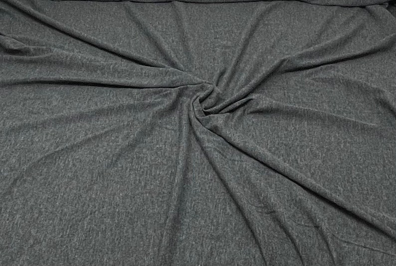May include: Close-up of a dark grey fabric with a textured, slightly speckled surface. The fabric is folded and draped, creating soft folds and wrinkles.