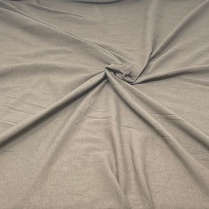 May include: A close-up of a smooth, light brown fabric with a wrinkled texture. The fabric is folded and draped, creating a soft, flowing look.