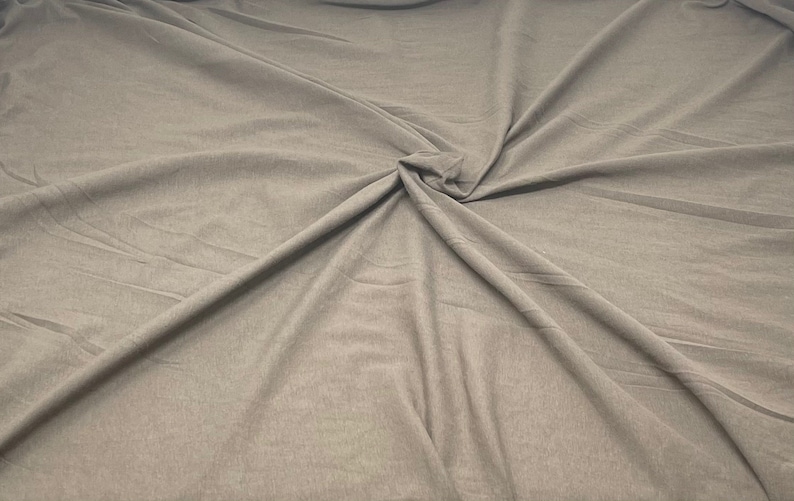 May include: A close-up of a smooth, light brown fabric with a wrinkled texture. The fabric is folded and draped, creating a soft, flowing look.