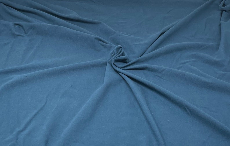 May include: A close-up of a smooth, blue fabric with a soft, wrinkled texture. The fabric is folded and draped, creating a sense of depth and dimension.