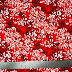 May include: Red fabric with a white and black floral pattern. The fabric is measured with a ruler.