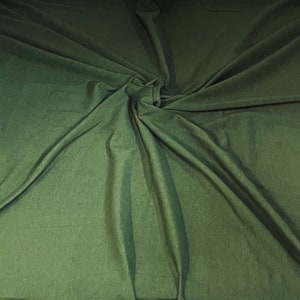 May include: A close-up of a green fabric with a soft, smooth texture. The fabric is draped and folded, creating a swirling pattern.