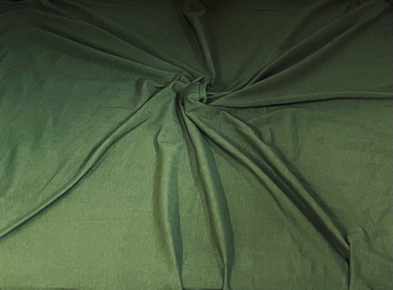 May include: A close-up of a green fabric with a soft, smooth texture. The fabric is draped and folded, creating a swirling pattern.