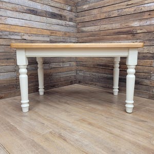 May include: A rectangular dining table featuring a natural light brown wood grain top and four off-white painted legs. The legs have a turned, rounded design with a tapered base. The table frame is finished in the same off-white colour as the legs.
