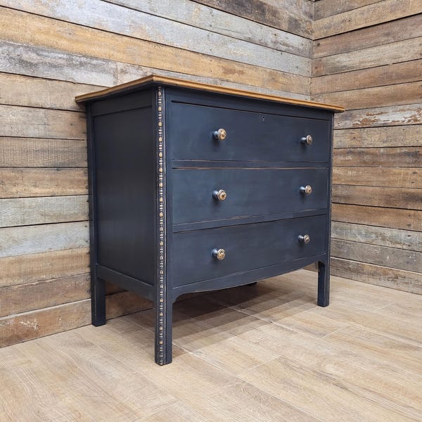 Cómoda de tres cajones con acabado envejecido, de madera pintada de negro, estilo antiguo.