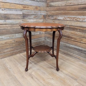 May include: A small, antique wooden side table with a round top and a lower shelf. The table has ornate, curved legs and a dark brown finish. The table is approximately 71 cm tall.