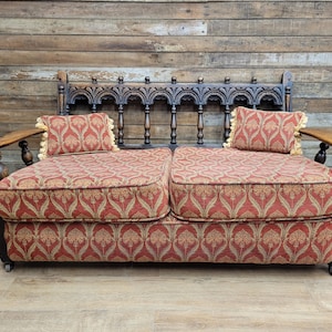 May include: A classic two-seater sofa with a dark wood frame and an elaborate back design. The cushions and pillows display a red and gold floral pattern. The sofa has rounded armrests and decorative tassels.