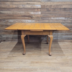 May include: A light brown wooden table with a rectangular top and four curved legs. The table has a drawer and is made of wood. The table is approximately 91 cm long and 61 cm wide.