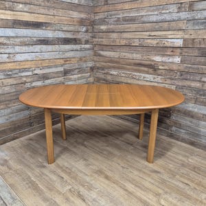 May include: Oval wooden dining table with four legs. The table is a light brown colour and appears to be made of wood. The table is approximately 152 cm long and 102 cm wide.