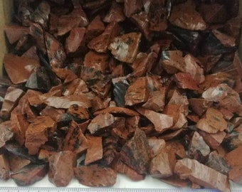Puede incluir: Primer plano de un montón de virutas de jaspe rojo y negro. Las virutas son de forma y tamaño irregulares, y algunas tienen una franja blanca que las atraviesa. Las virutas están dispuestas sobre una superficie blanca con una regla marcada en pulgadas.