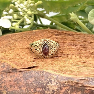 Può includere: Un anello d'oro con una pietra preziosa rossa incastonata in un design a filigrana.