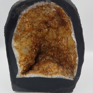 May include: A geode with a black exterior and a large, open cavity filled with clear quartz crystals with brown inclusions.