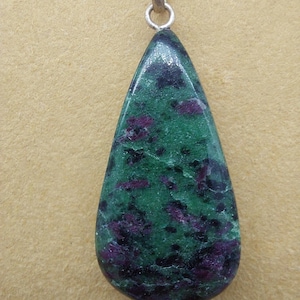 Pode incluir: Um pingente em forma de lágrima com uma gema verde e roxa. A gema tem um padrão manchado de verde, roxo e preto.