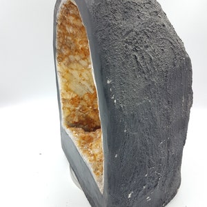 May include: A black geode with a large opening revealing a cluster of clear and amber-colored crystals inside.