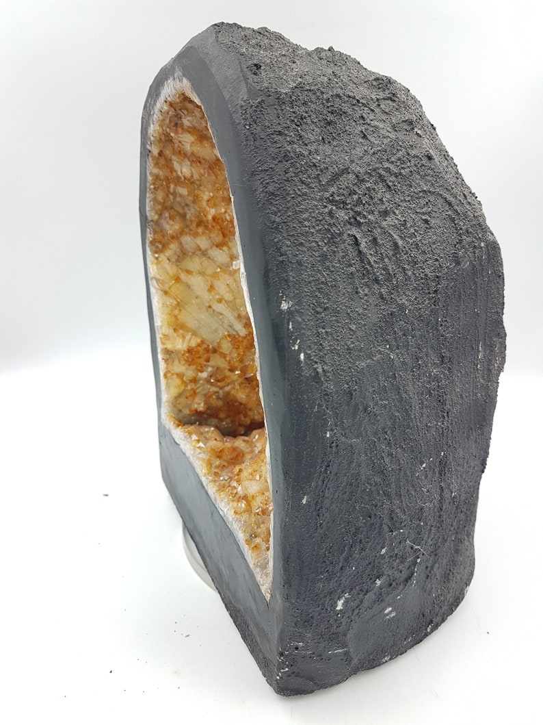 May include: A black geode with a large opening revealing a cluster of clear and amber-colored crystals inside.