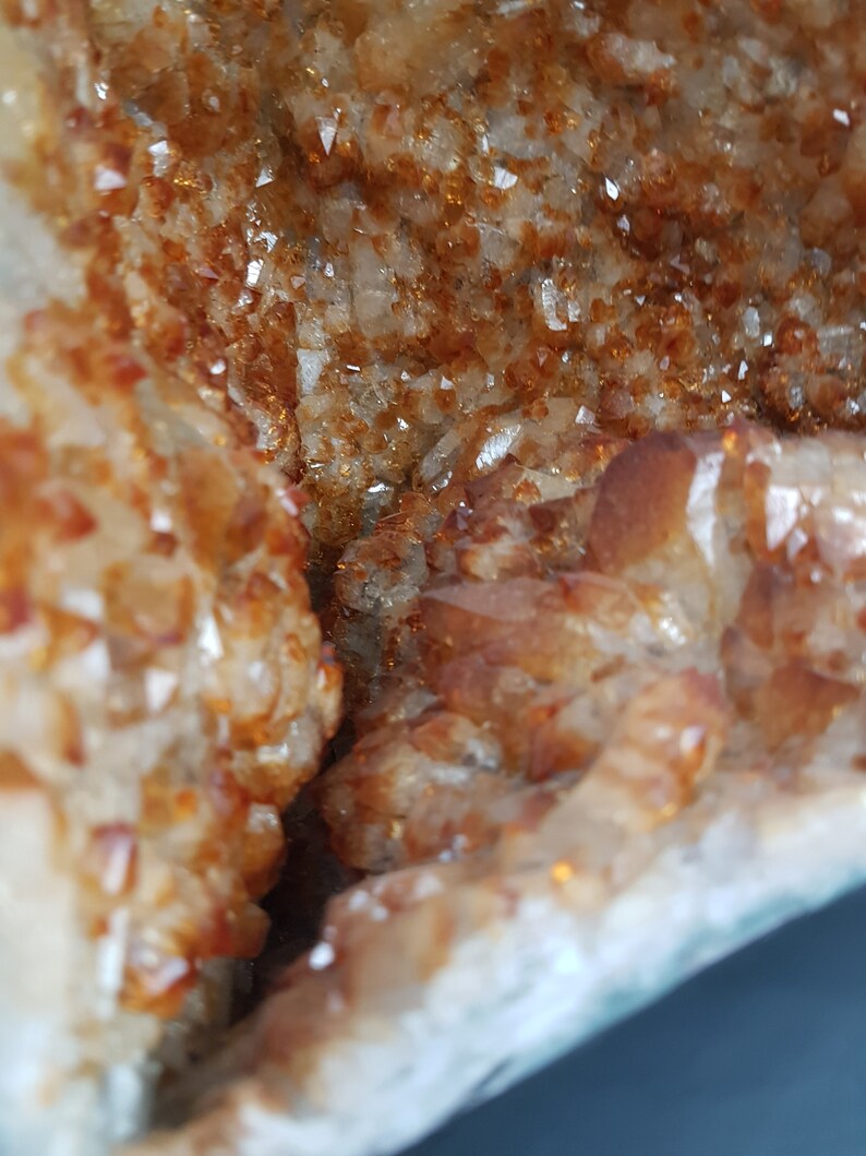 May include: Close-up of a natural crystal geode with a rough, textured exterior and a sparkling, translucent interior. The geode is filled with small, orange-brown crystals.