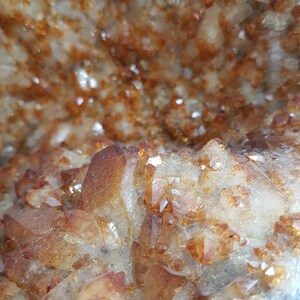 May include: Close-up of a geode with a cluster of small, clear, and amber-colored crystals. The crystals are arranged in a random pattern, creating a natural and organic look.